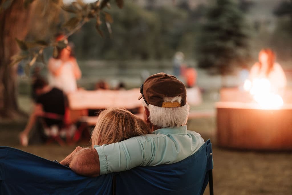 A couple sitting close together watching the fire pit glow at dusk during a Locals Night evening