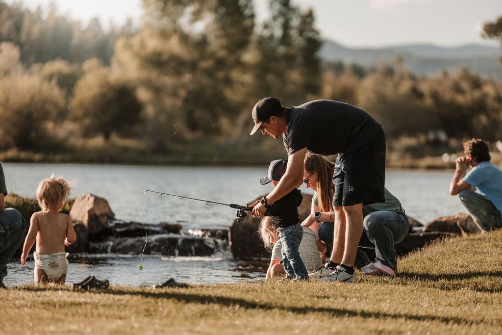 A family casting a line together at the water's edge in the golden evening light