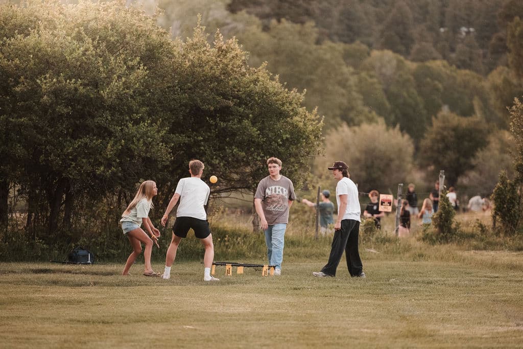 Teens playing lawn games together on the grass near the tree line at sunset