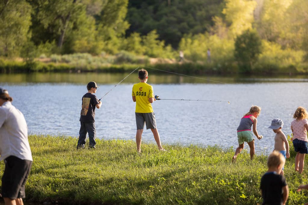 Kids casting their lines and playing along the grassy bank of the pond in the golden evening light