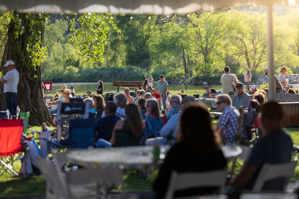 Guests seated in the shade with the pond and green tree line beyond, taking in the evening from under the tent