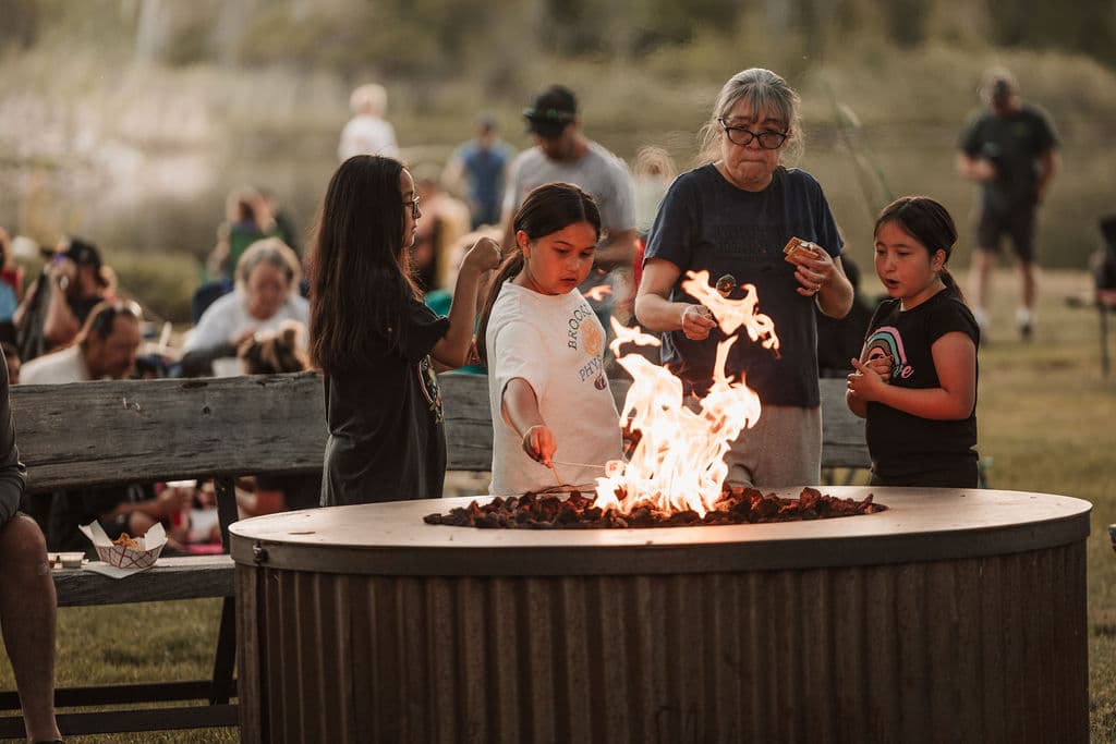 Children and family roasting marshmallows around the communal fire pit at twilight