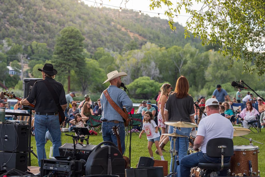 The band playing from behind the stage as guests listen from their lawn chairs with the foothills rising beyond the pond