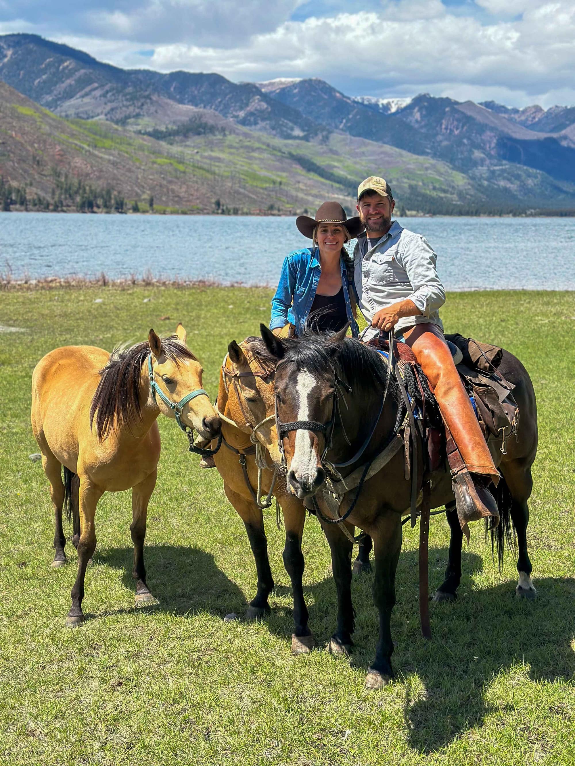 Paul and Krii Black on horseback by a mountain lake with snow-capped San Juan peaks