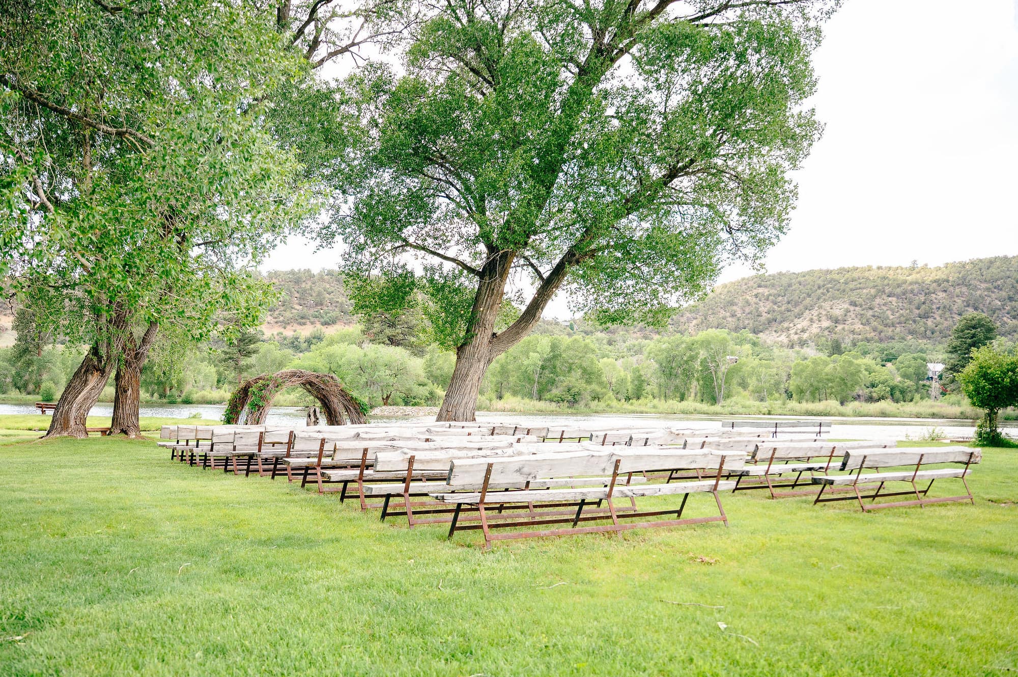The ceremony site at LePlatt's Pond with rustic log benches, woven branch arbor, cottonwood trees, and mountain backdrop