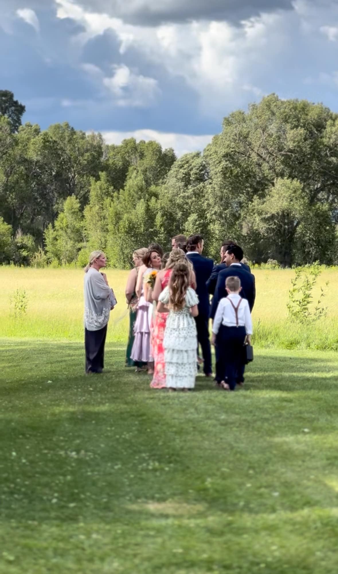 Day-of coordinator Lacy organizing the bridal party lineup on the ranch lawn with cottonwood trees and Colorado sky behind