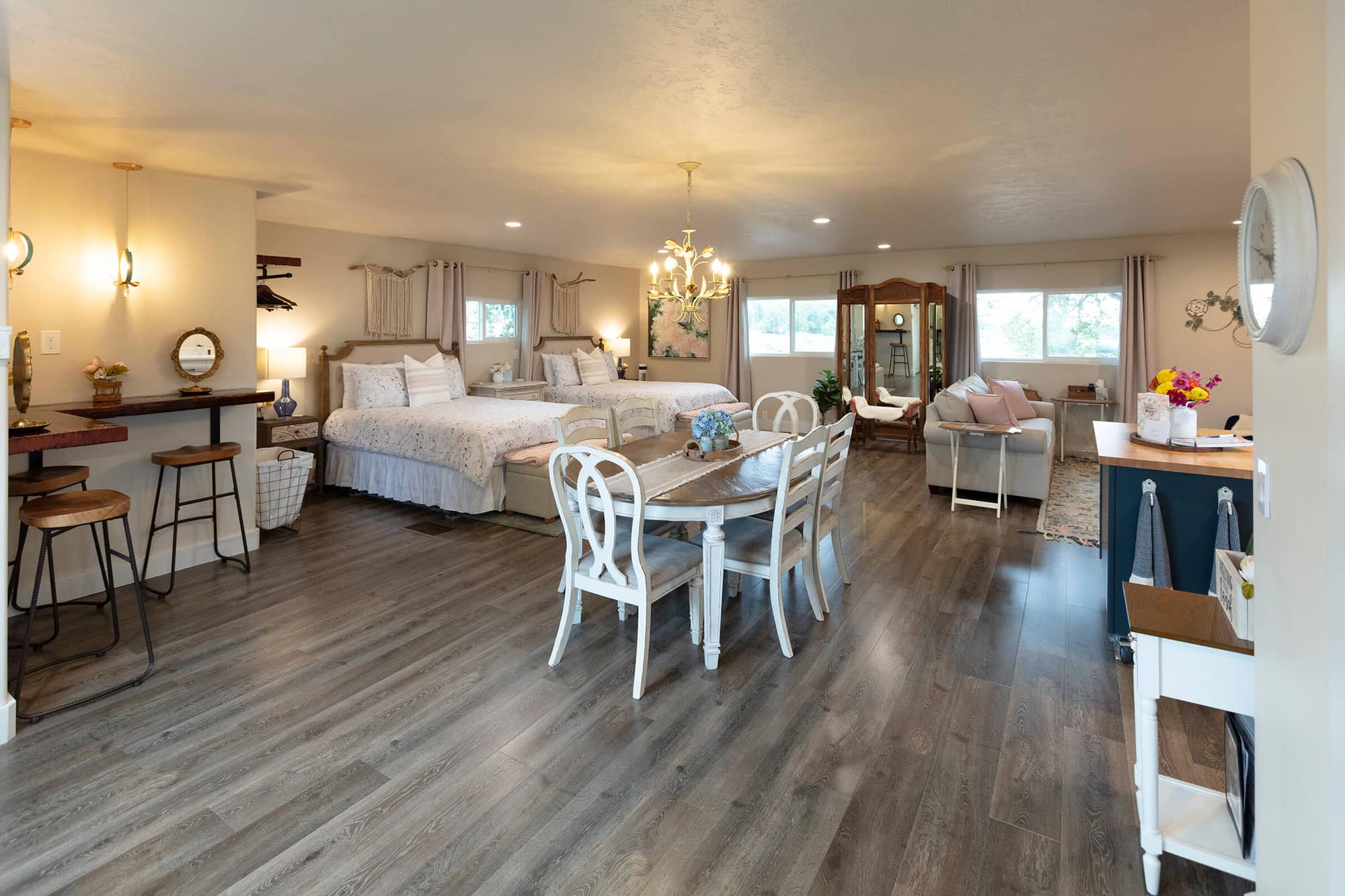 The Loft bridal suite interior with two queen beds, gold chandelier, bridal bar with stools, farmhouse dining table, and cozy seating area near large windows