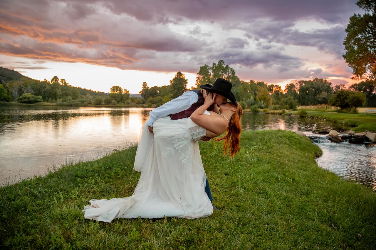 Laura and Nathan sharing a dramatic dip kiss by the pond at sunset with a purple and pink sky