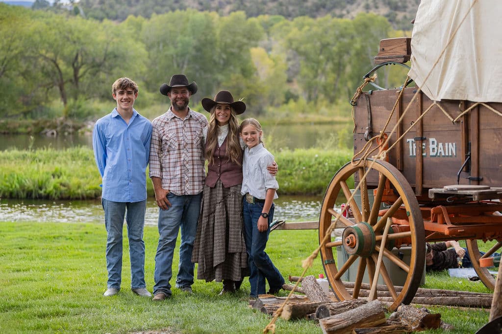 Family standing beside a historic chuckwagon beside the pond