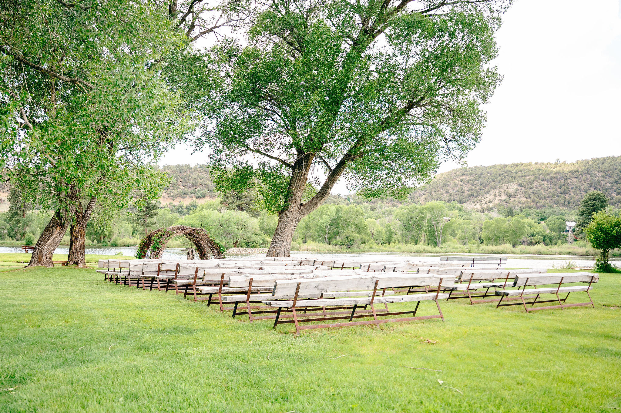 Lakeside ceremony site at LePlatt's Pond with rustic log benches, woven branch arch, and cottonwood trees by the water