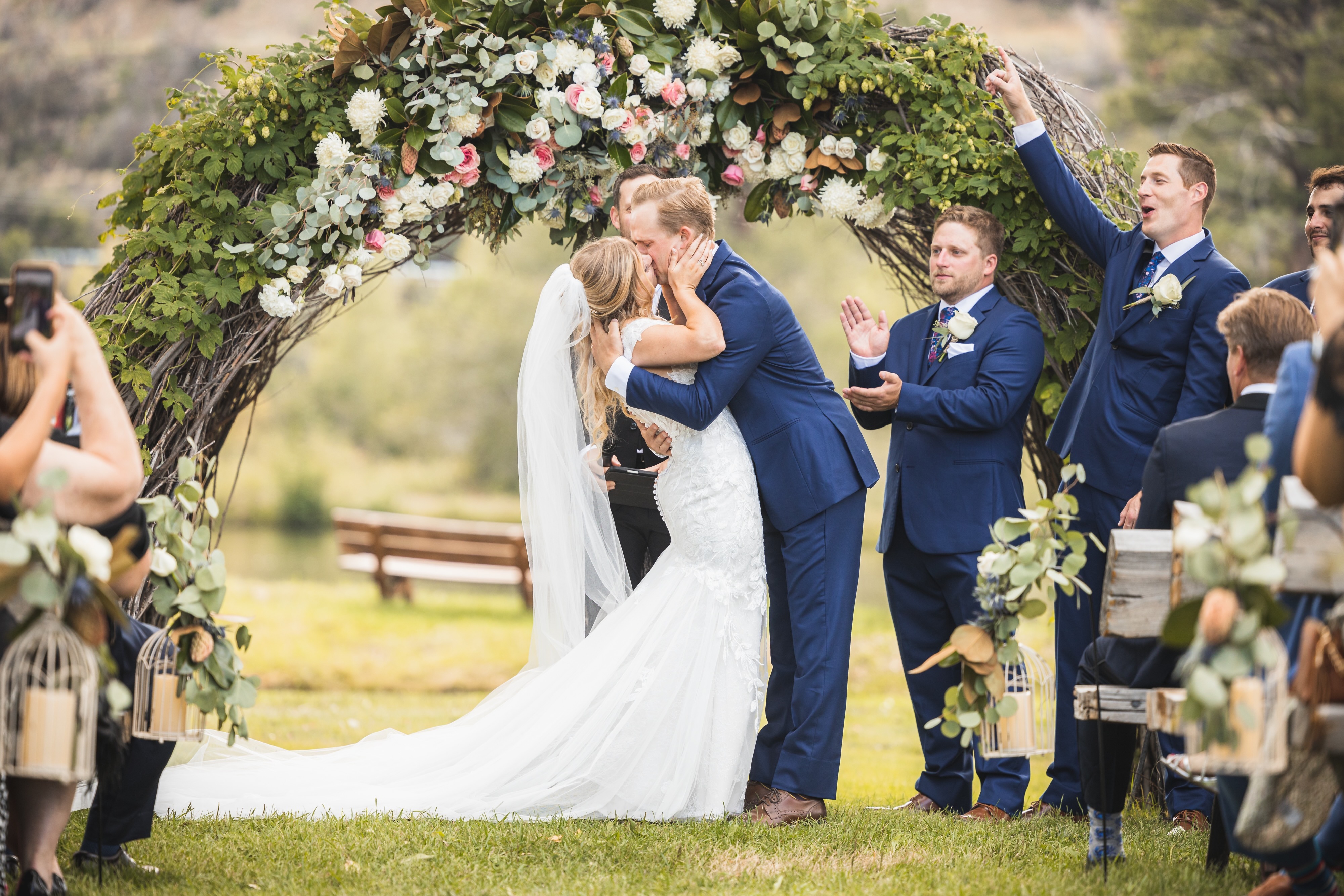 Bride and groom sharing their first kiss under a floral arbor at a lakeside ceremony at LePlatt's Pond