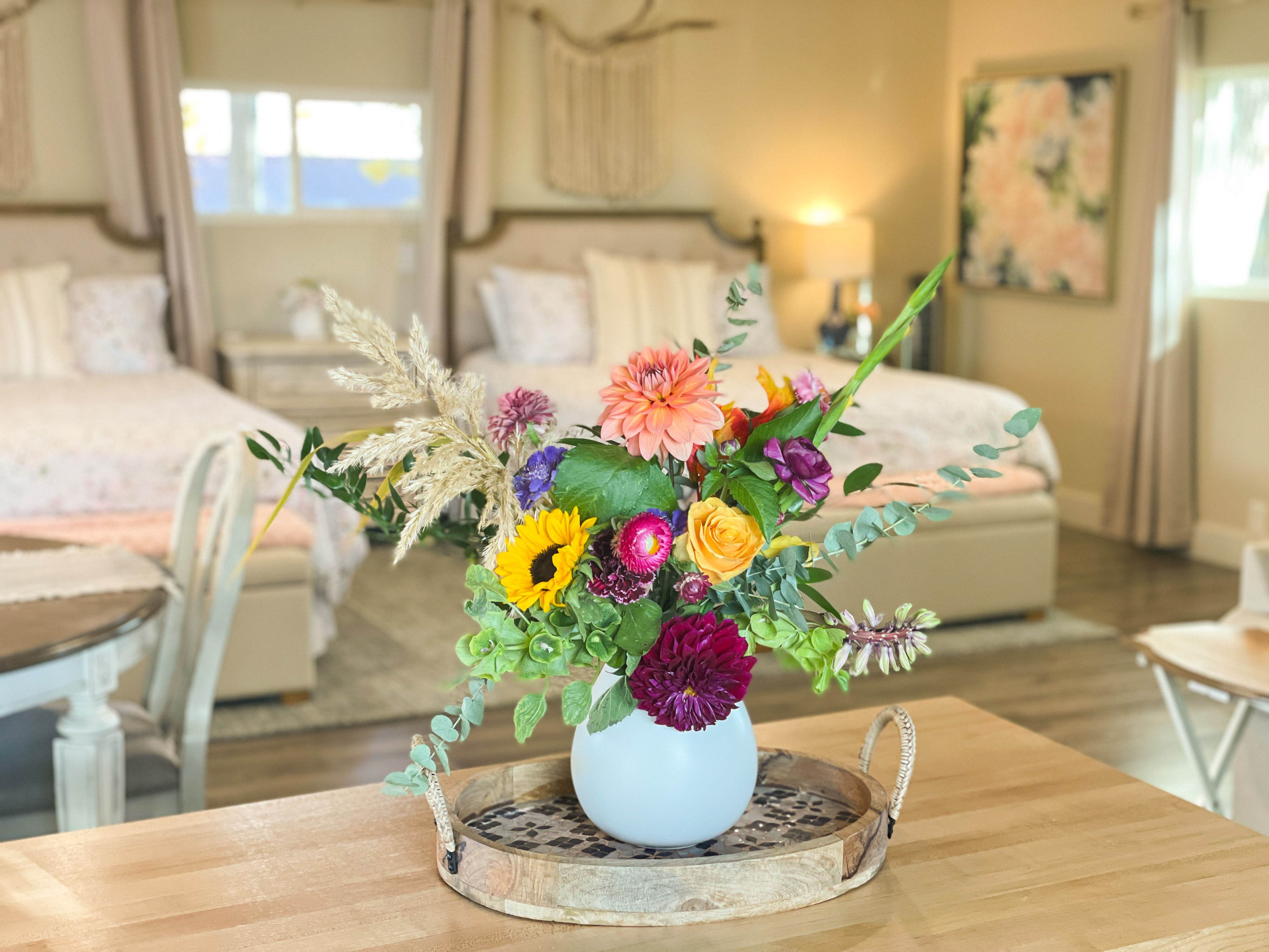 Farm-fresh flower bouquet with sunflowers, dahlias, and roses on the butcher block island with two queen beds softly blurred in the background