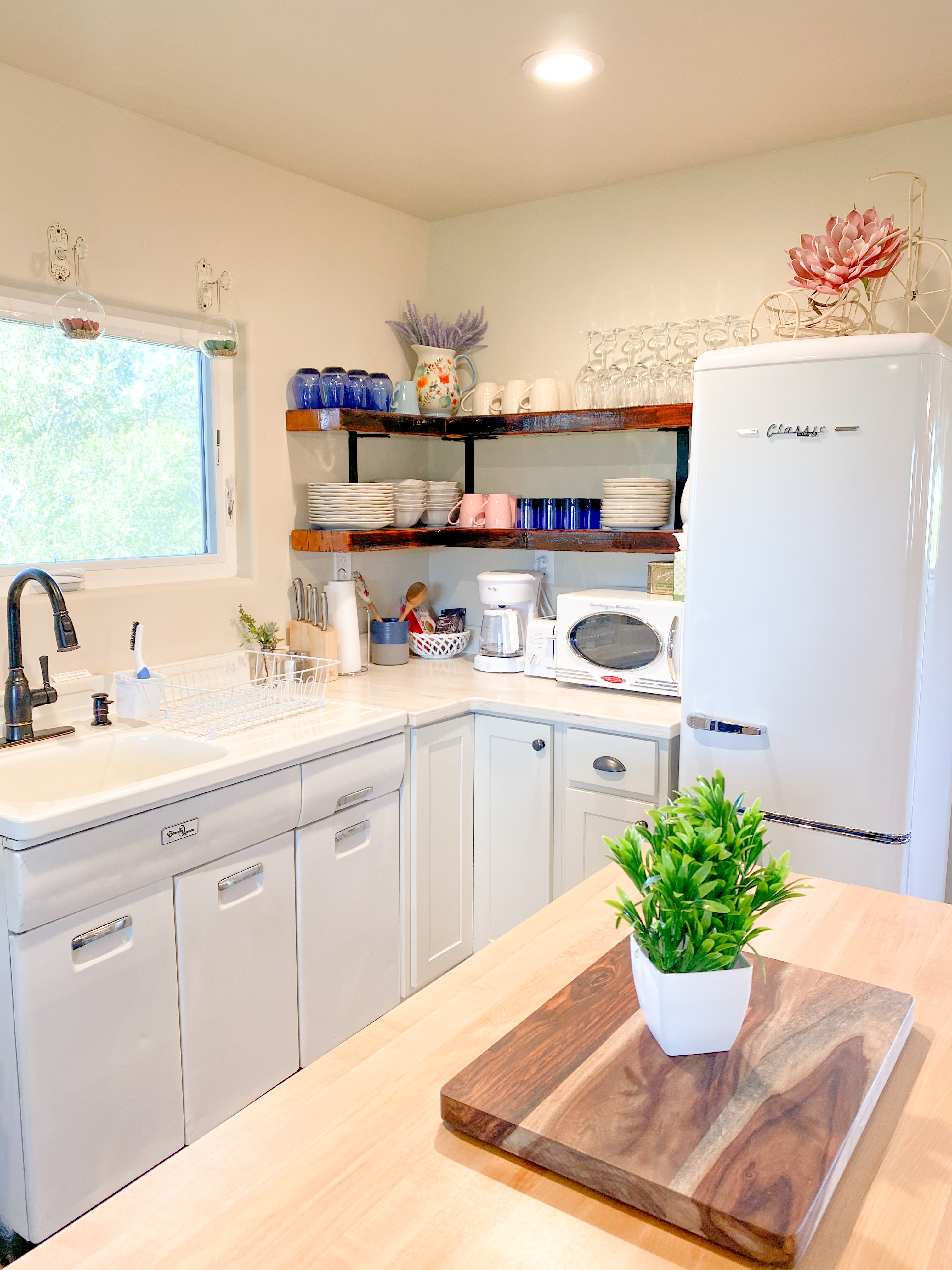 The Loft kitchen with white retro fridge, open wooden shelving with colorful dishes, farmhouse sink, and butcher block island