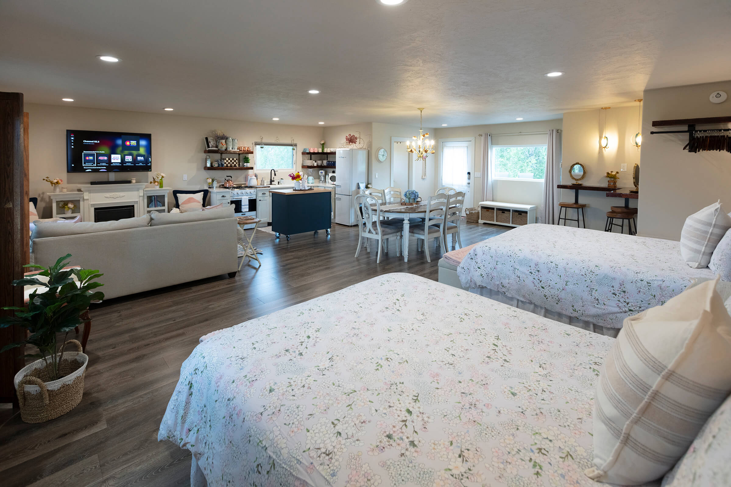 The Loft wide-angle view showing two queen beds, living area with TV and fireplace, blue kitchen island, dining table, and bridal bar