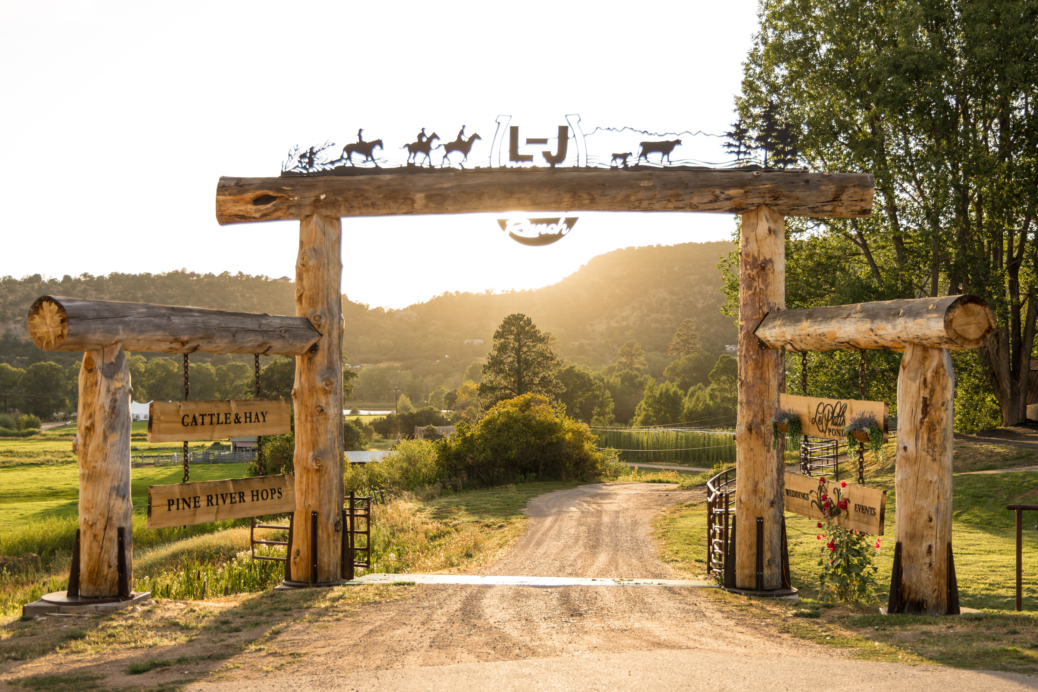 L-J Ranch log entrance gate with metal silhouette artwork at sunset